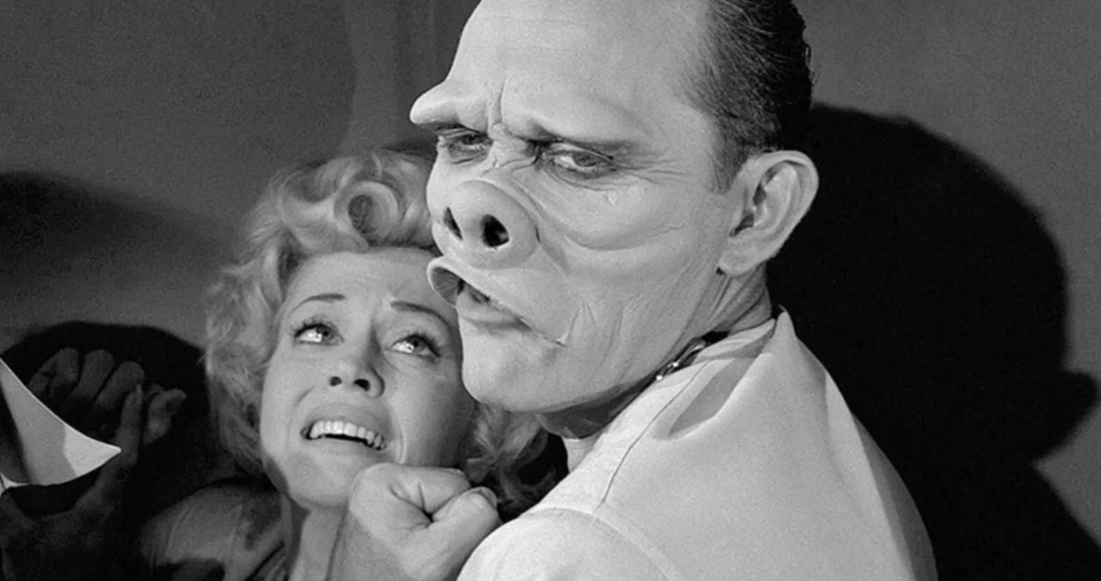 Image from "The Eye of the Beholder," an episode of the original "The Twilight Zone" -- the imprisoned victim of a series of plastic surgery experiments to make her face conform to the social norms is restrained by her surgeon, a piglike humanoid